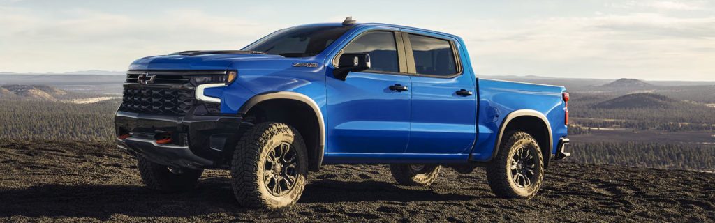 Blue Chevrolet Silverado 1500 parked on rugged terrain with a mountainous background.
