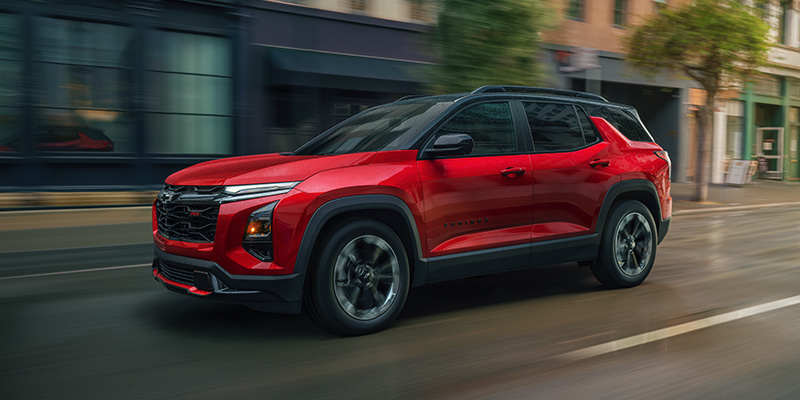 Red Chevrolet Equinox driving through a city street with modern buildings in the background.