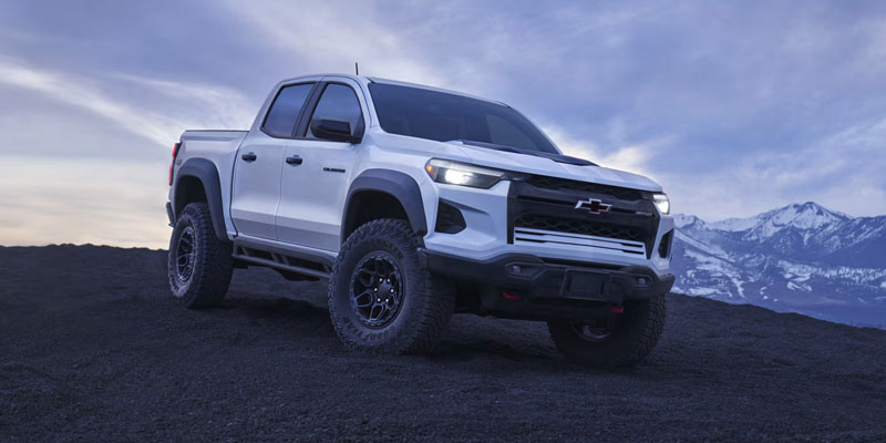 White Chevrolet Colorado pickup truck on a mountain landscape.
